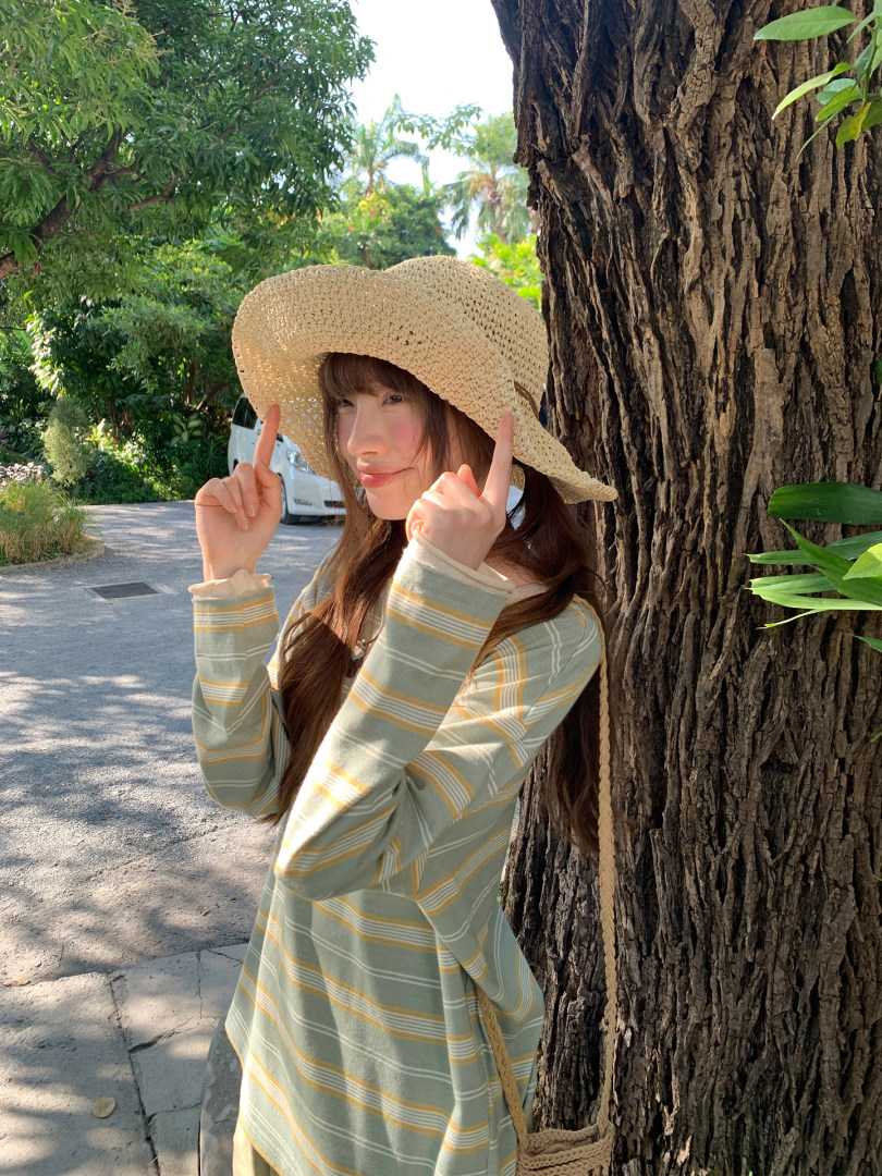 Woman wearing a striped green long-sleeve top and straw hat outdoors