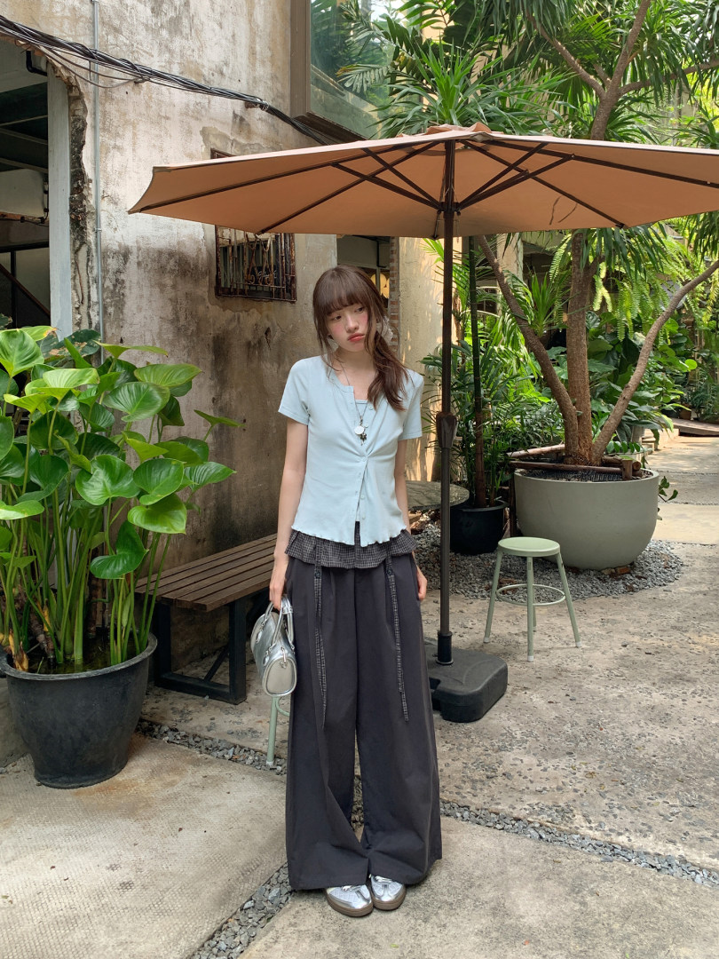 Young woman wearing a light blue button-front top with wide dark pants outdoors