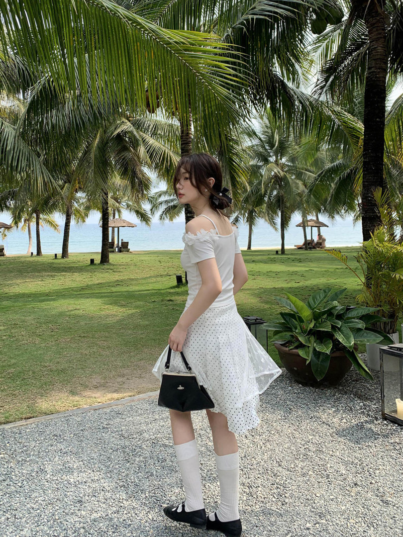 Woman wearing a white off-shoulder top and polka dot skirt at a tropical beach