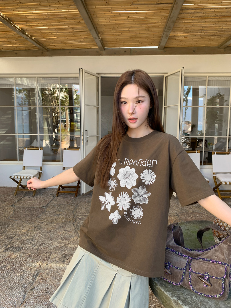 Model wearing a brown graphic short-sleeve T-shirt with a floral print and light pleated skirt