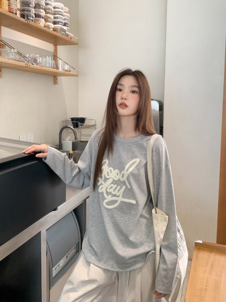 Woman wearing a gray long-sleeve graphic top with "good day" text