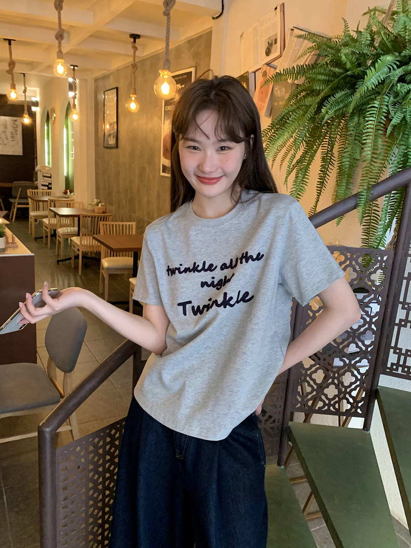 Person wearing a gray graphic T-shirt with black text in a cafe