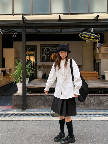 Woman wearing a white oversized blouse with a black skirt, hat, socks, and shoes