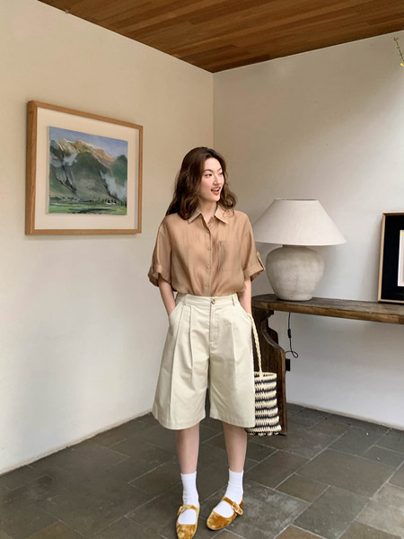 Model wearing a beige short-sleeve button-up shirt with cream pleated shorts