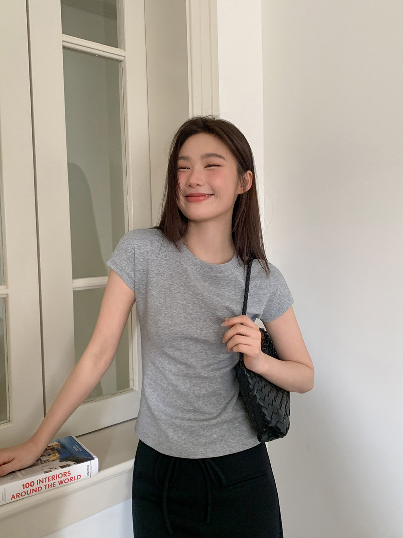 Woman wearing a gray short-sleeve T-shirt with a black woven shoulder bag
