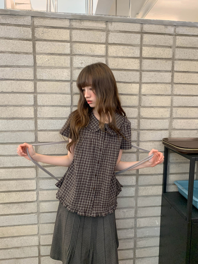 Model wearing a brown plaid short-sleeve button-up top with a gray pleated skirt