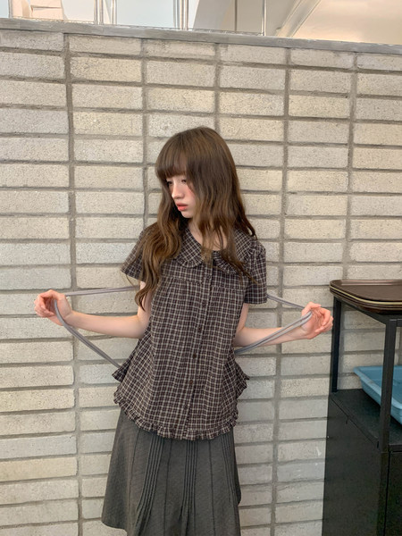 Model wearing a brown plaid short-sleeve button-up top with a gray pleated skirt