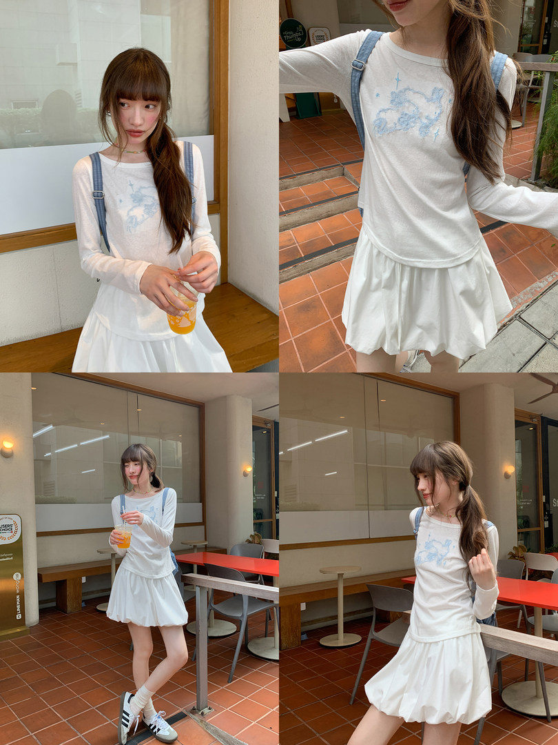 Woman modeling a white long-sleeve top with a blue graphic and a white skirt