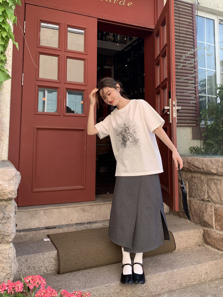 Model wearing a white graphic T-shirt with a gray midi skirt and black Mary Jane shoes