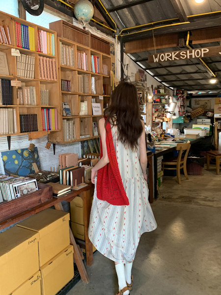 Woman wearing a white striped dress with red floral accents and a red woven shawl in a workshop