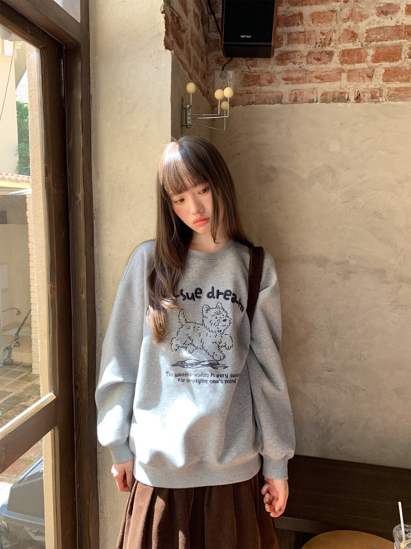 Woman wearing a gray graphic sweatshirt and brown skirt indoors