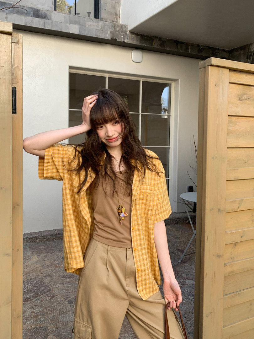 Model wearing a yellow plaid short-sleeve shirt over a brown top with tan pants