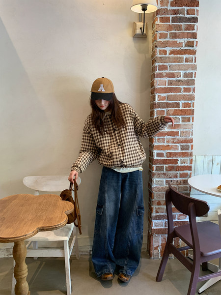 Model wearing a brown checkered jacket with wide-leg jeans and a baseball cap