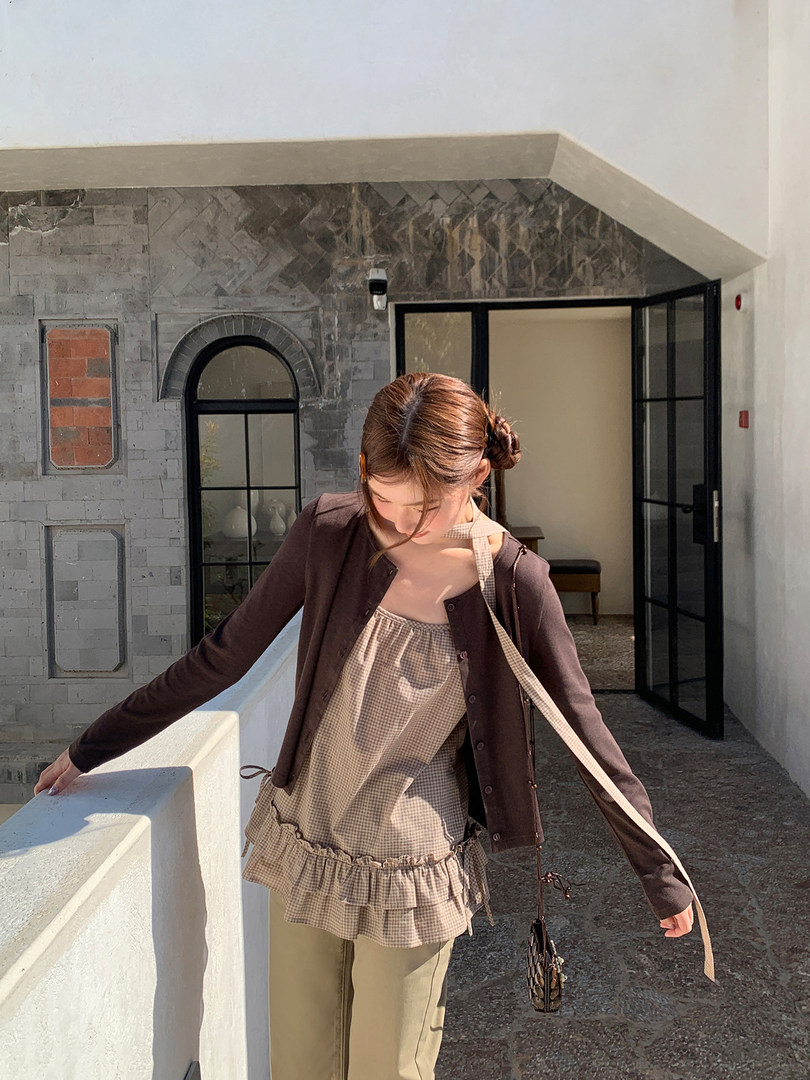 Woman wearing a brown cardigan over a gingham ruffled top and beige pants