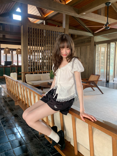 Woman wearing a white puff-sleeve blouse and black shorts in a resort-style setting