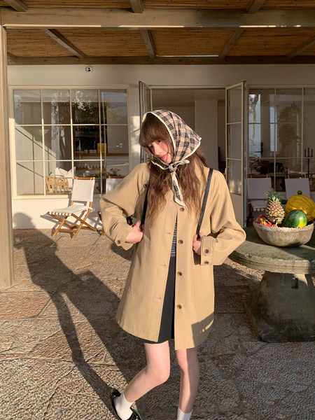 Woman wearing a beige button-front coat with a plaid headscarf outdoors