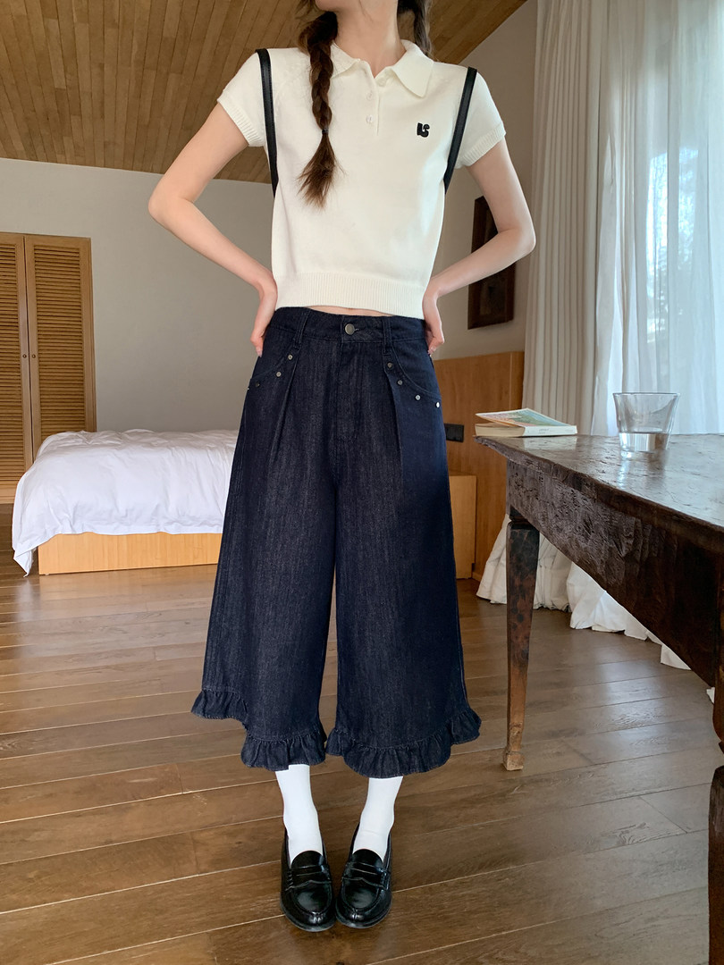 Model wearing a white short-sleeve polo knit top with dark wide-leg denim pants and loafers