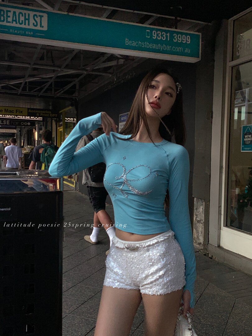 Woman wearing a blue long-sleeve fitted top and white sequin shorts on a city street
