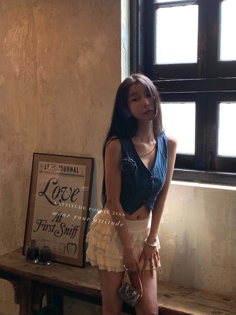 Model wearing a blue sleeveless denim-style top and a white ruffled mini skirt