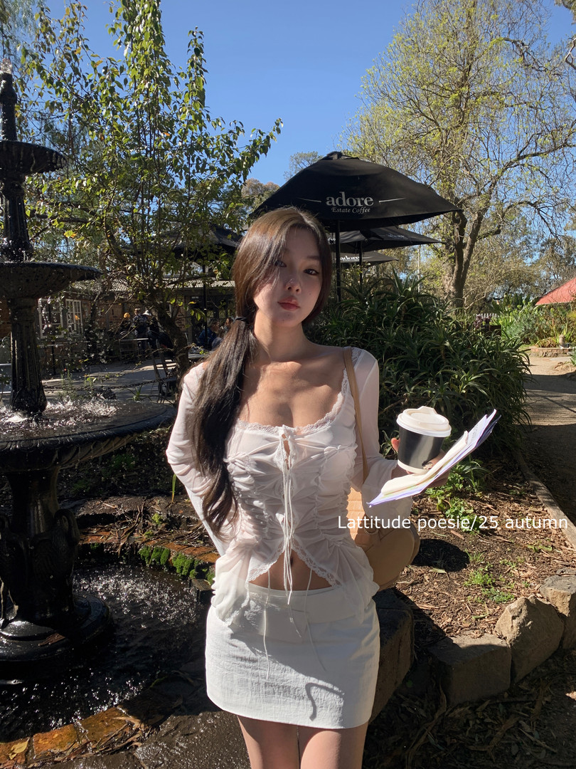 Model wearing a white ruched lace-trim long-sleeve top and matching mini skirt outdoors