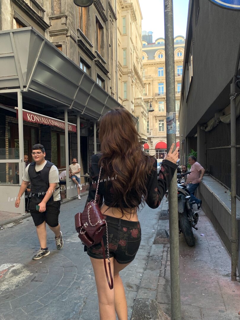 Woman wearing a black crop top and shorts with a burgundy chain-strap handbag on a street