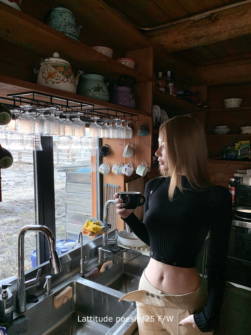 Woman wearing a black ribbed cropped top and beige pants in a kitchen