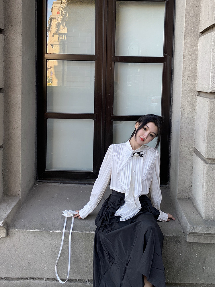 Woman wearing a white long-sleeve bow blouse and black skirt outdoors