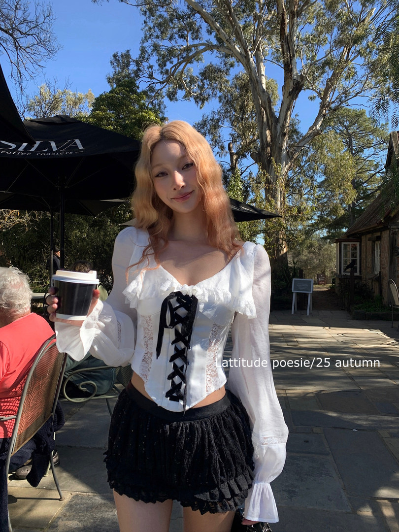 Woman wearing a white lace-up blouse with black ruffled shorts outdoors