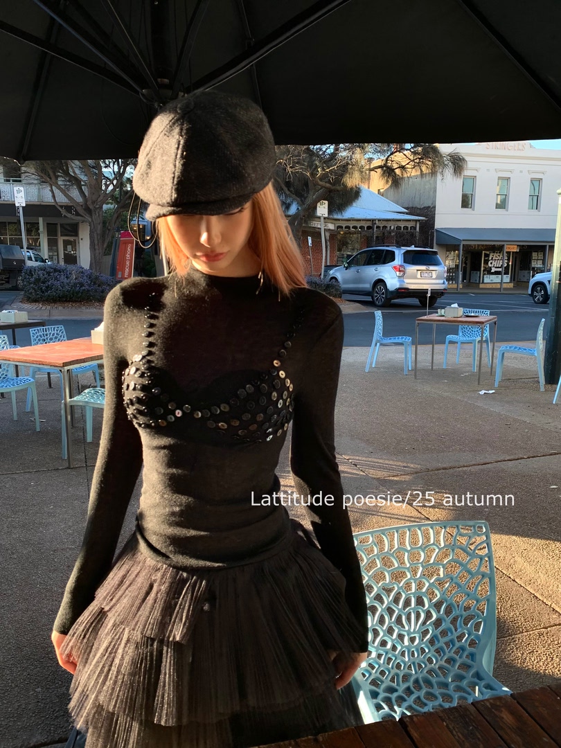 Model wearing a black sheer embellished top and pleated skirt outdoors