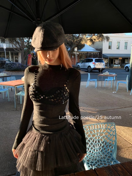 Model wearing a black sheer embellished top and pleated skirt outdoors