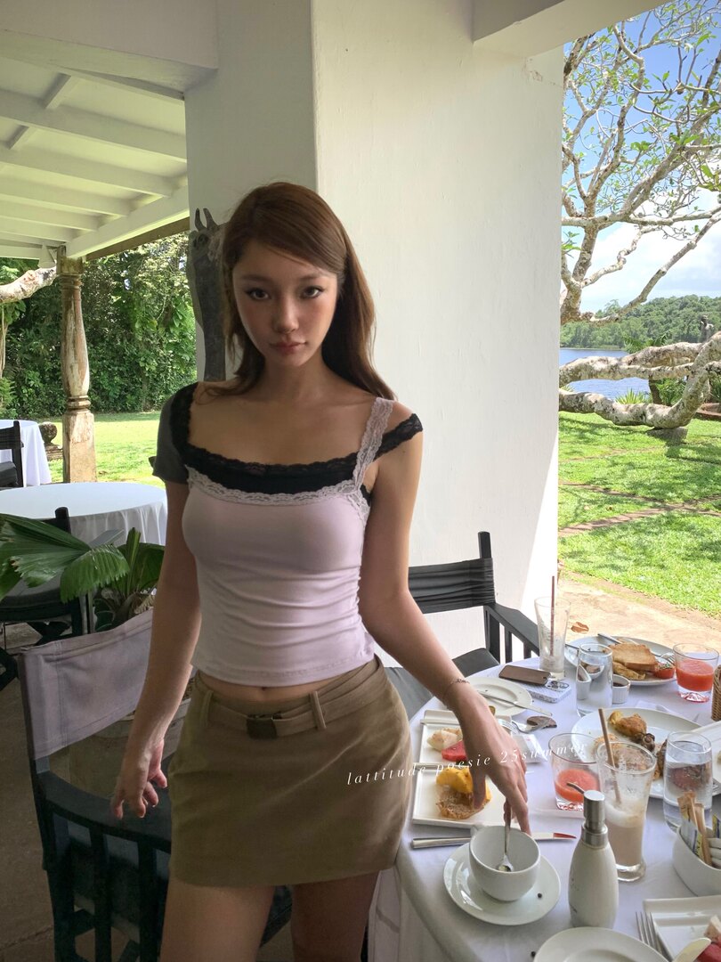 Woman wearing a lilac lace-trim camisole and tan mini skirt at an outdoor resort dining area