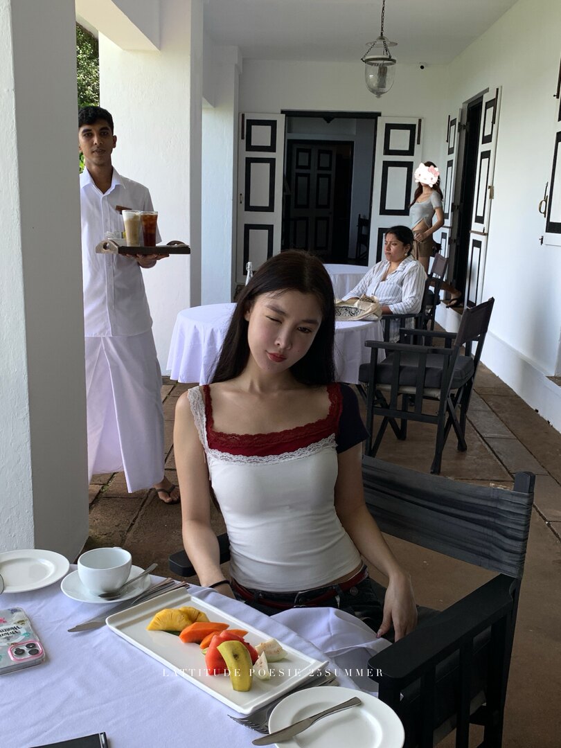White camisole top with red lace trim worn by a model at a café