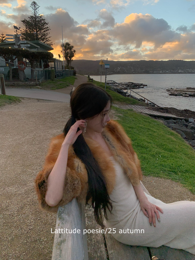 Woman wearing a cream dress with a brown fur shawl by the seaside at sunset