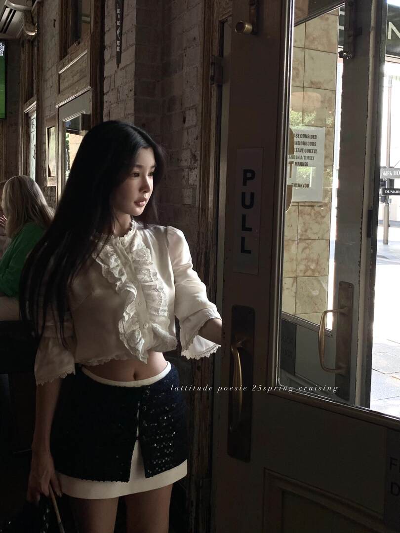 Model wearing a white ruffled blouse with a dark mini skirt
