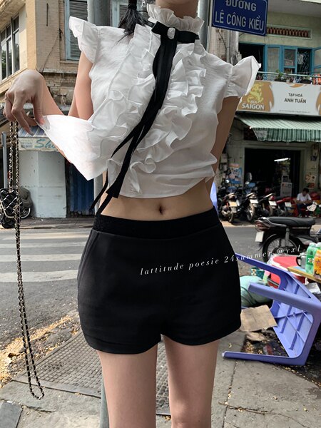 Model wearing a white ruffled sleeveless top with black shorts outdoors