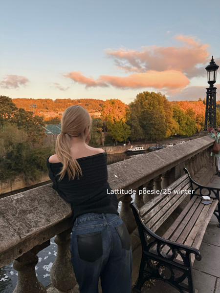 Woman wearing dark jeans and a black off-shoulder top while leaning on a bridge
