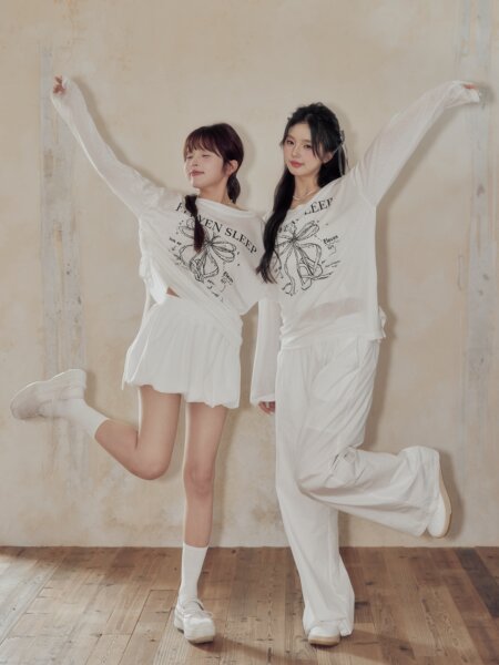 Two models wearing matching white loungewear sets with graphic long-sleeve tops and relaxed pants
