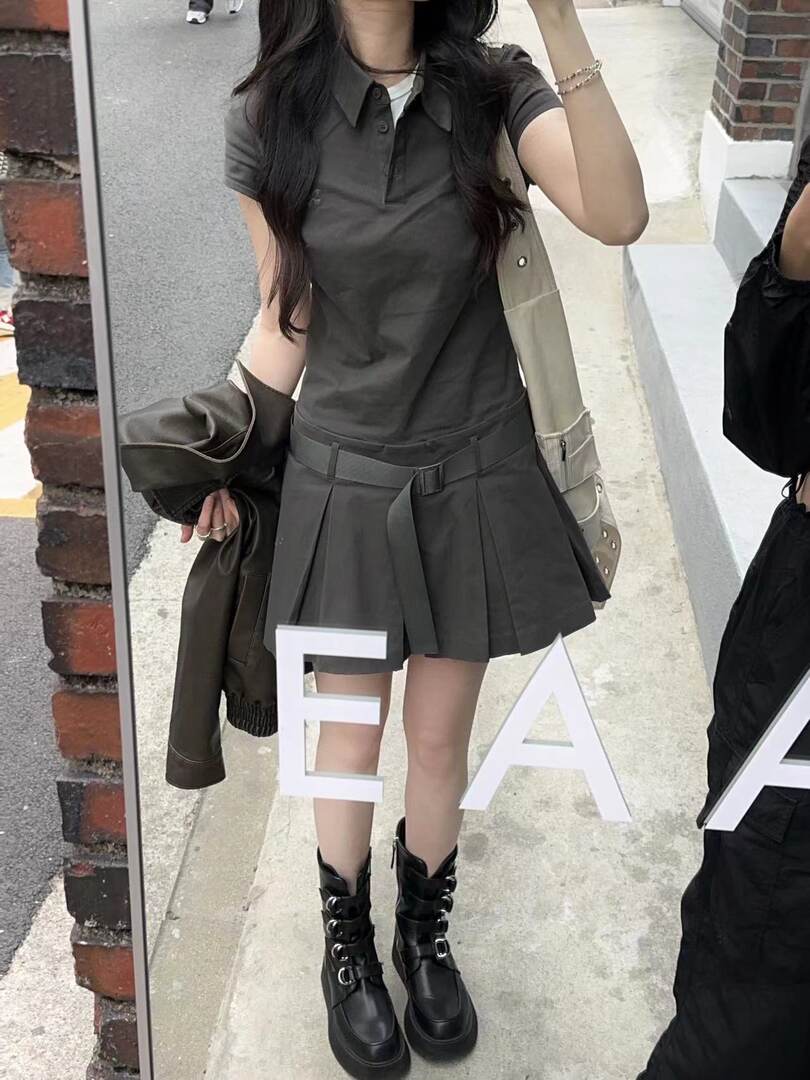 Woman wearing a dark gray polo top, pleated mini skirt, and black buckled boots in a mirror selfie