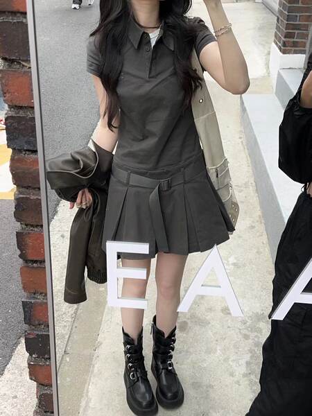Woman wearing a dark gray polo top, pleated mini skirt, and black buckled boots in a mirror selfie