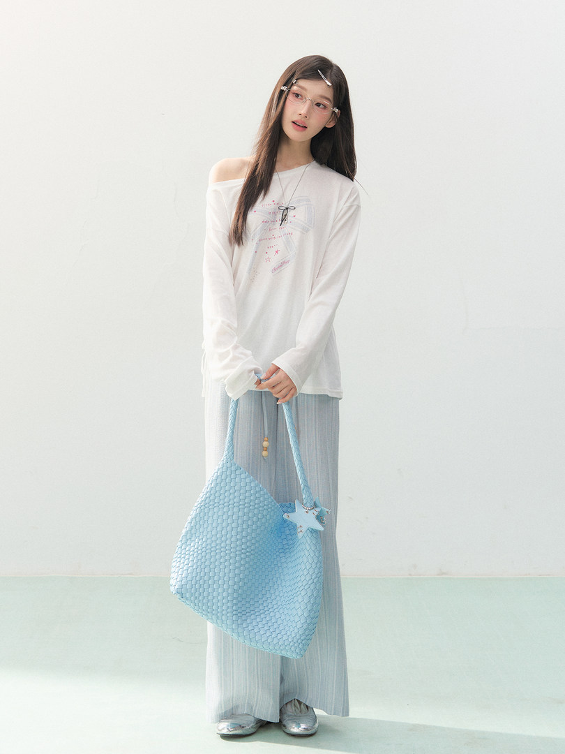 Model wearing a white long-sleeve top and holding a light blue woven tote bag