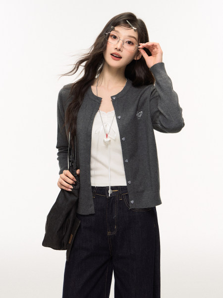 Female model wearing a dark gray cardigan over a white top with dark jeans and glasses