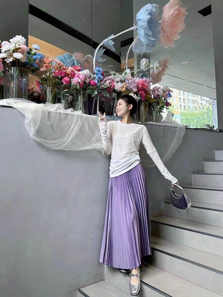 Model wearing a white long-sleeve floral top with a lavender pleated skirt
