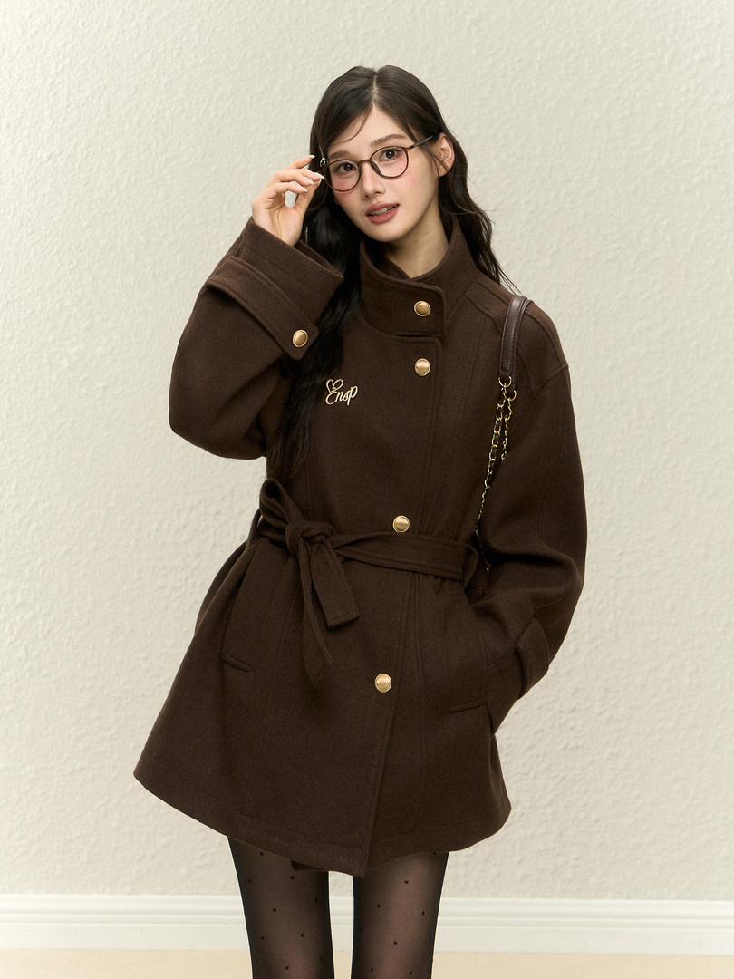 Brown belted coat worn by a model with gold buttons and glasses