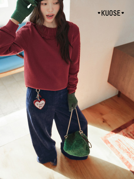 Model wearing a burgundy knit sweater with navy pants and a green handbag