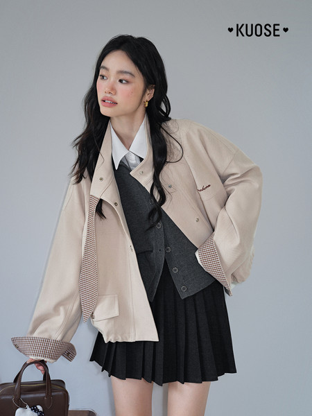 Model wearing a beige cropped jacket layered over a dark pleated skirt and shirt