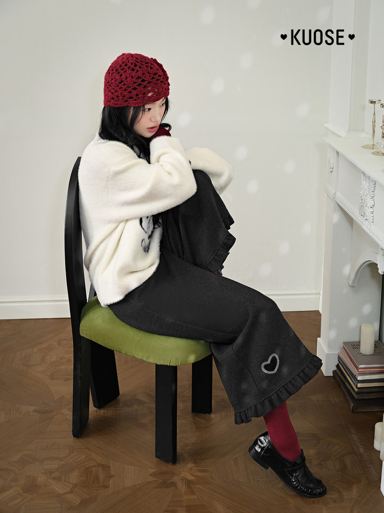 Model wearing a cream sweater with black pants and a red knit hat indoors