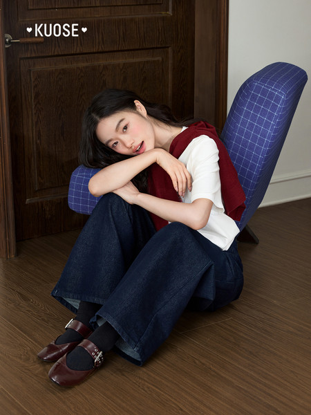 Model wearing a white top with a red sweater vest and wide-leg dark jeans