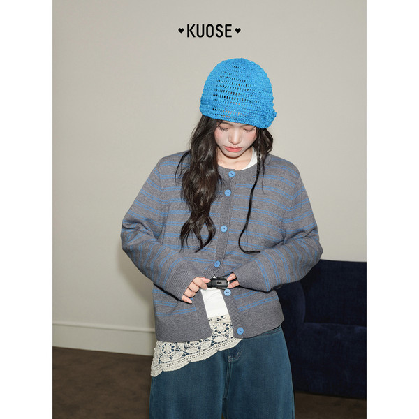 Model wearing a striped gray cardigan with a bright blue knit hat