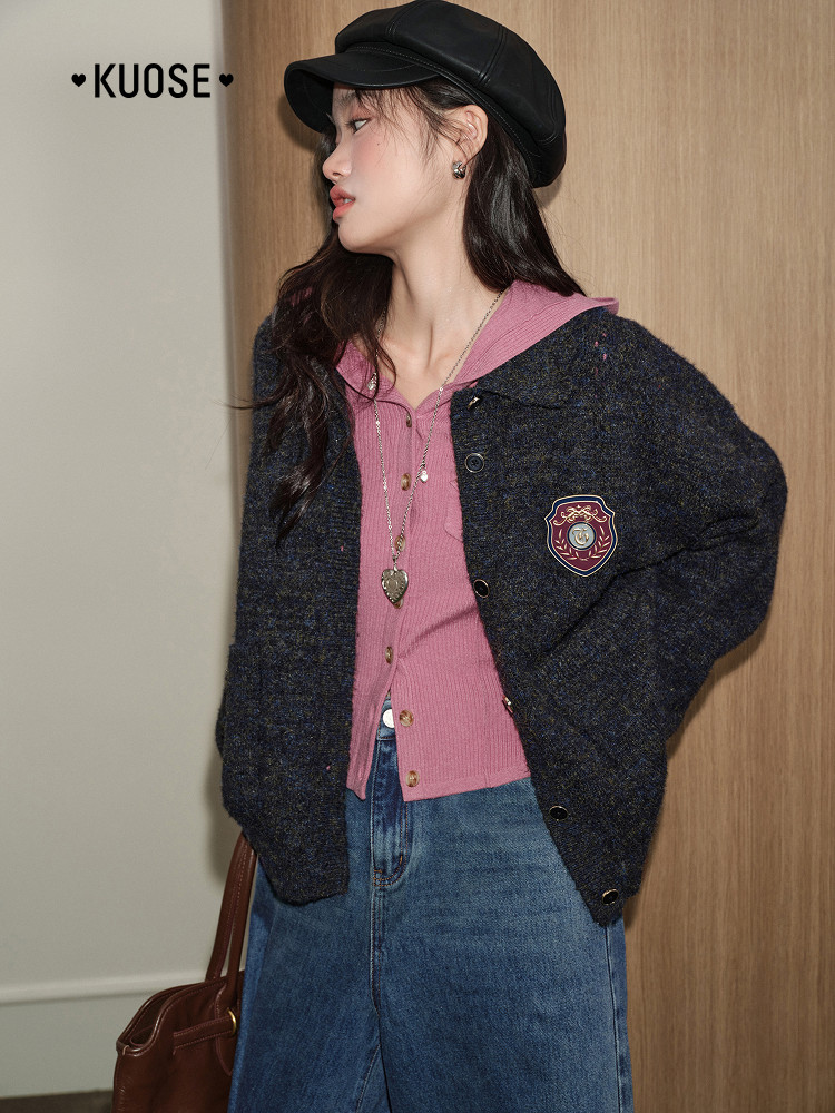 Female model wearing a dark cardigan jacket over a pink top and blue jeans with a black cap