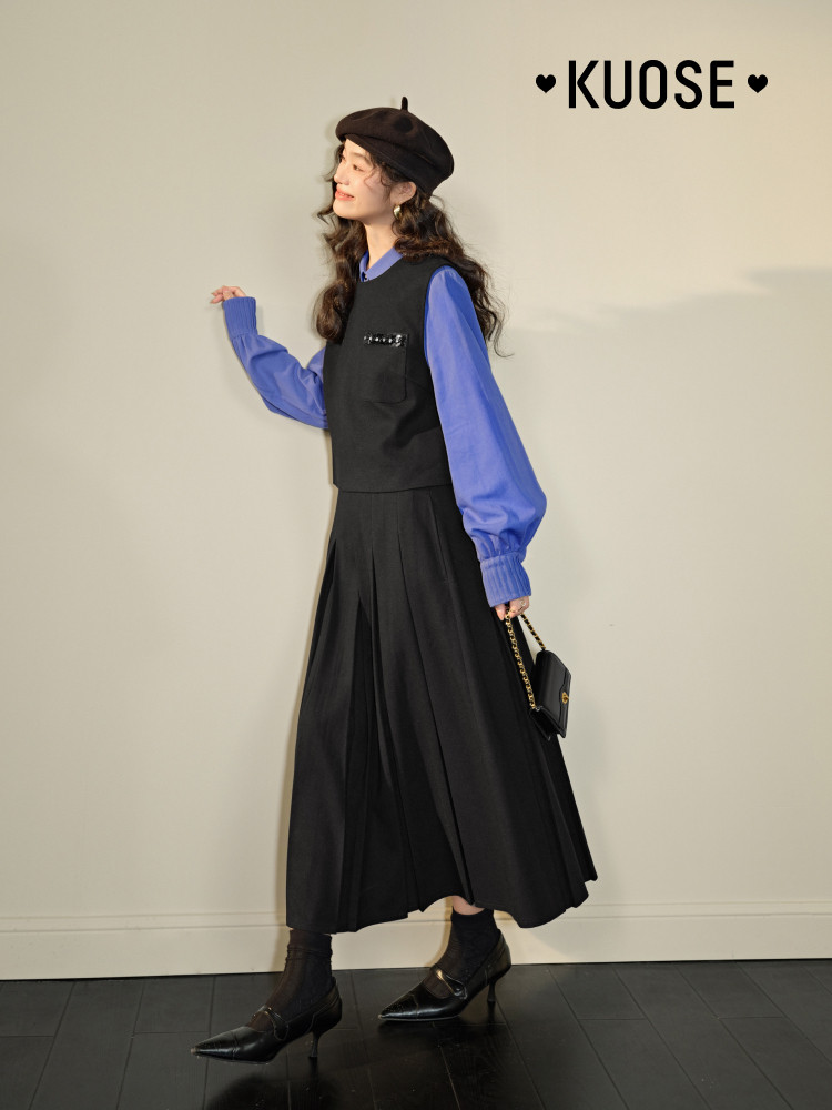 Model wearing a black layered dress outfit with blue sleeves, beret, and handbag